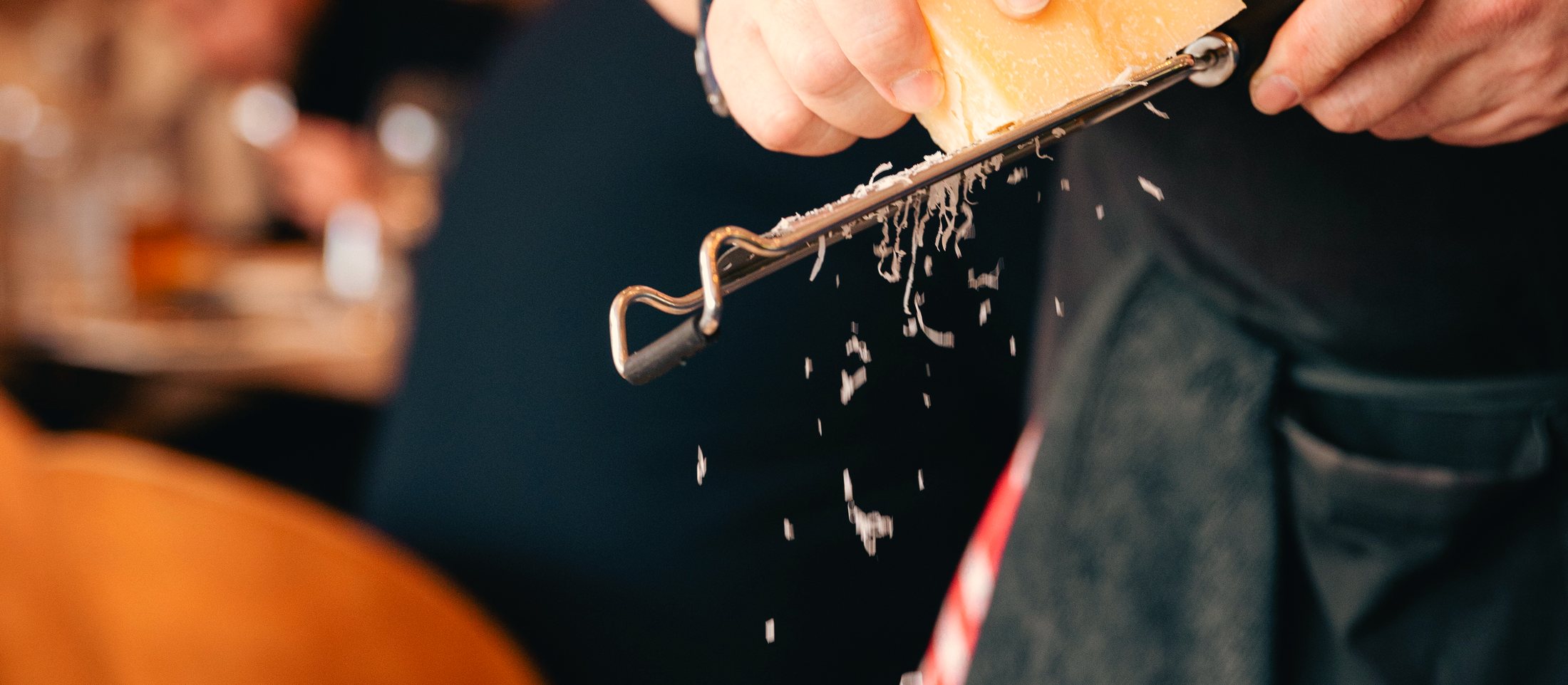 Le chef râpe du parmesan au-dessus d’une assiette, en pleine salle.