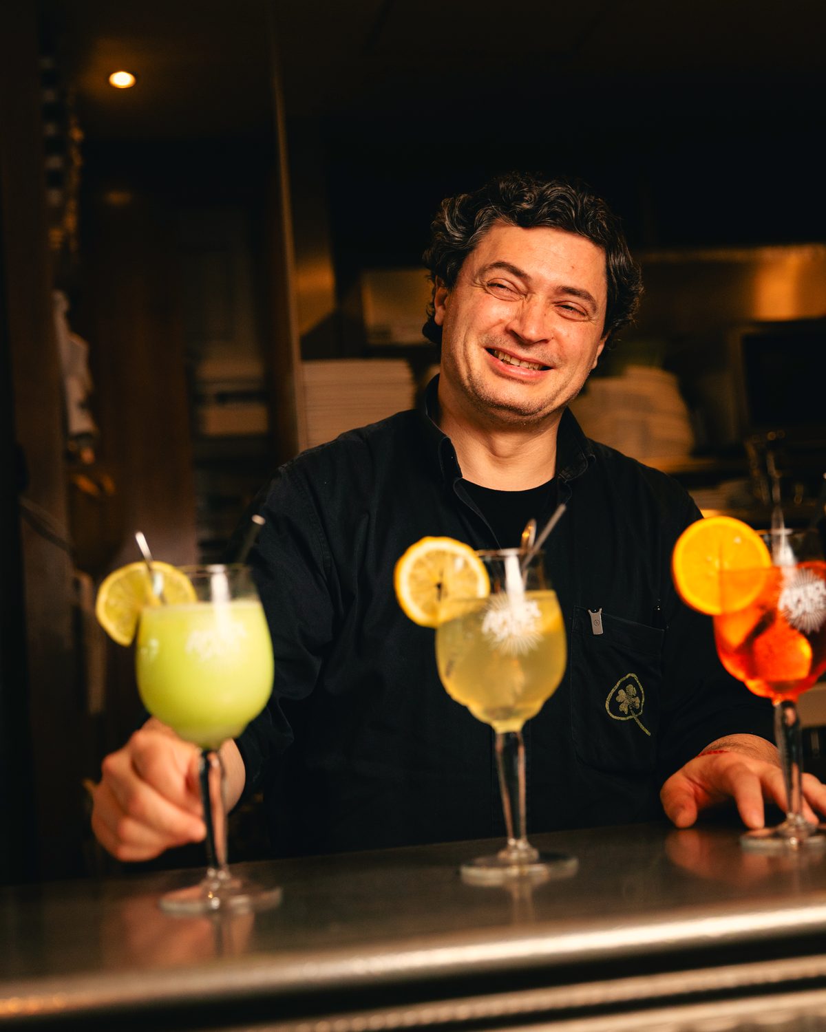 Membre de l’équipe souriant derrière trois cocktails posés au comptoir.