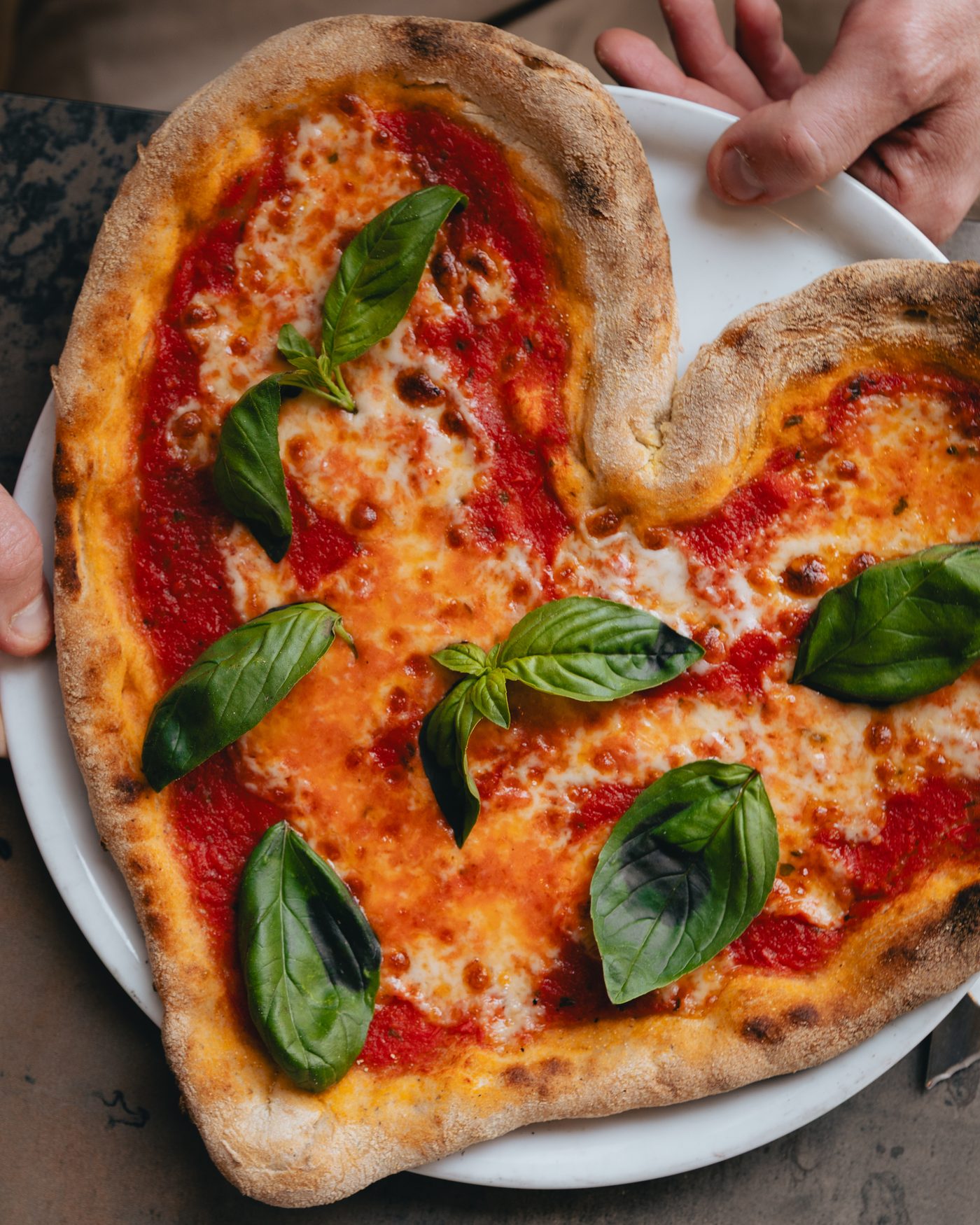Pizza margherita sans gluten en forme de cœur, basilic frais, servie à l’assiette.