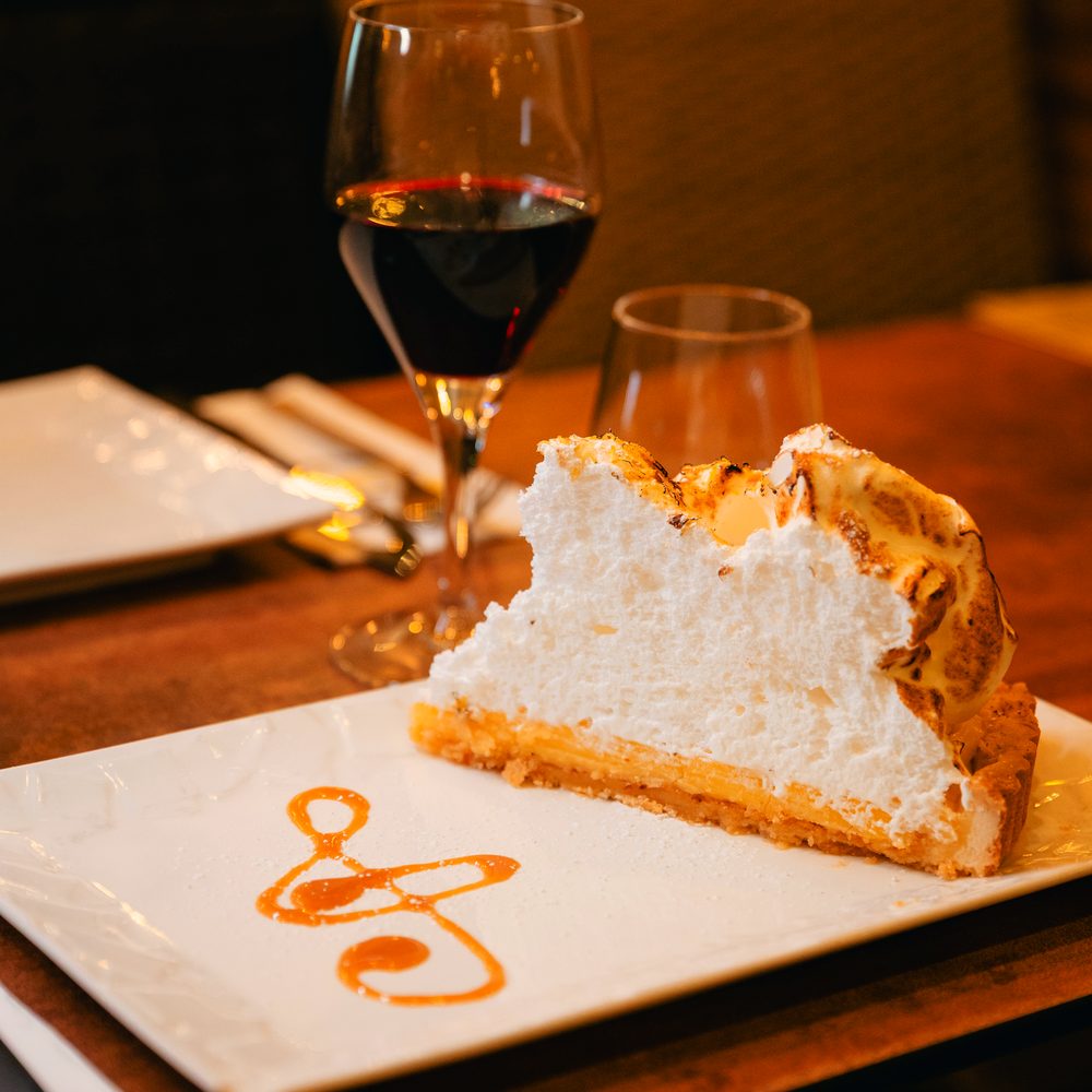 Part de tarte au citron meringuée servie à table avec un verre de vin rouge.